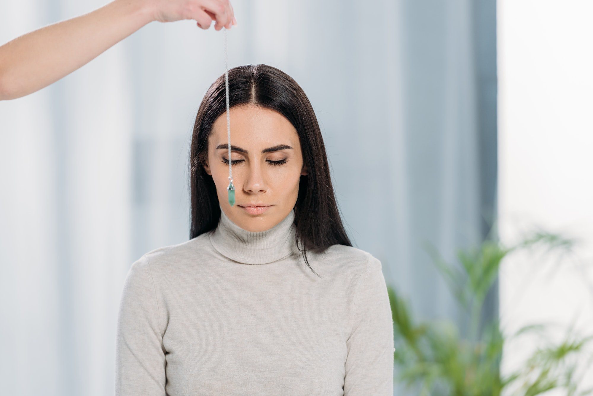 cropped shot of hypnotist with pendulum hypnotizing young woman with closed eyes