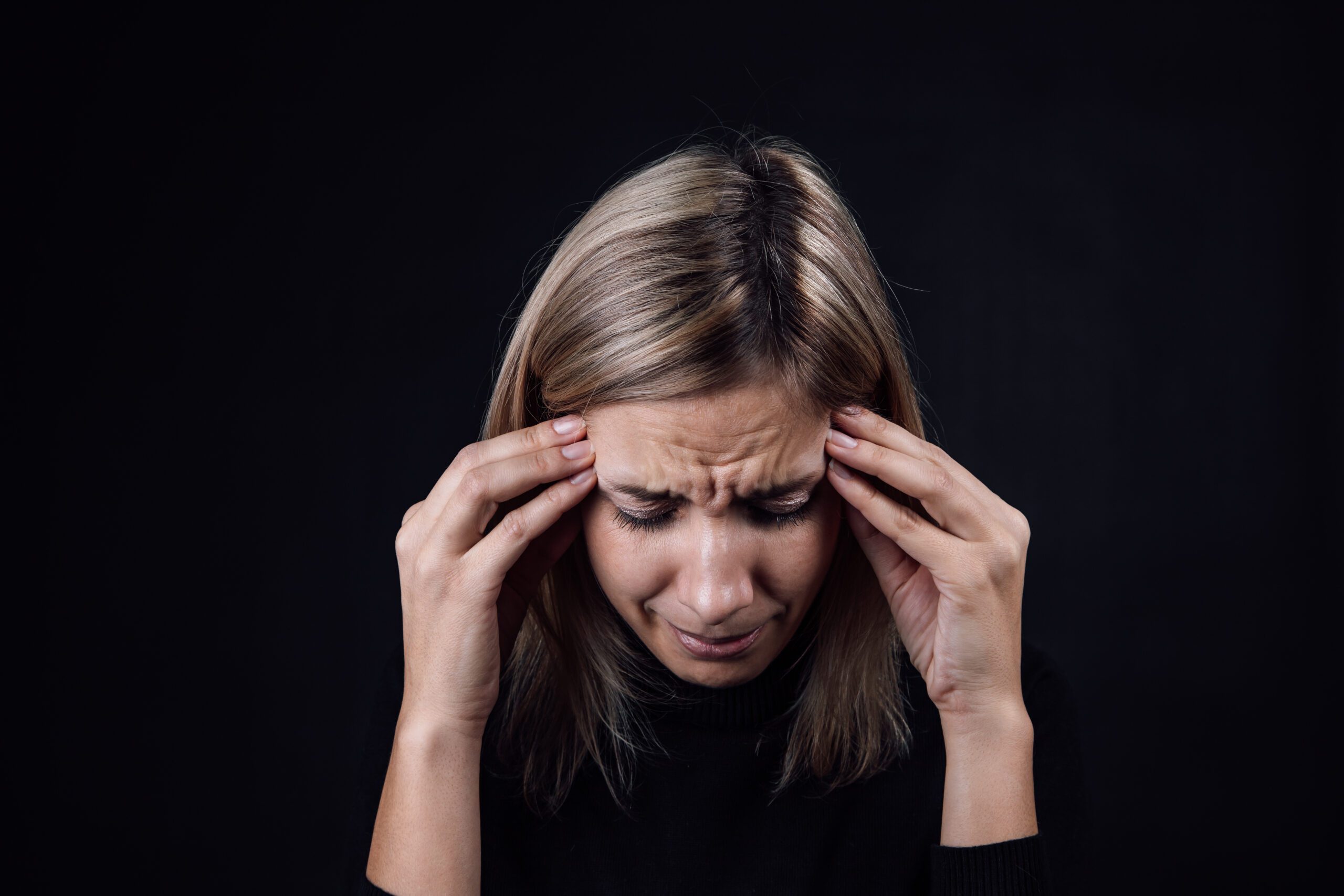 Portrait of crying woman with face down hand fingers touching temples on black background. Victim of