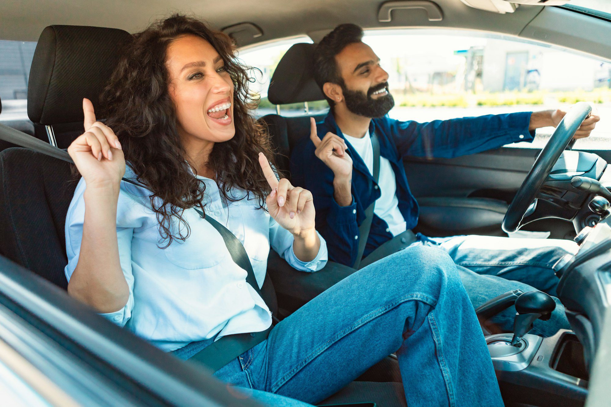 Emotional young arab couple guy and joyful lady listening to music and singing, enjoying their car
